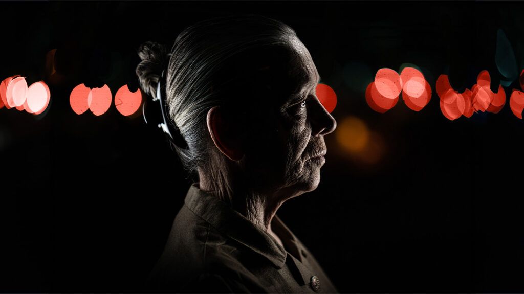 older woman with white hair seen in the dark from the profile