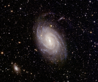 A magnificent spiral galaxy is visible in the center of this space image.  In the background there are many stars.  Towards the bottom left of the scene is a much smaller misty white patch.