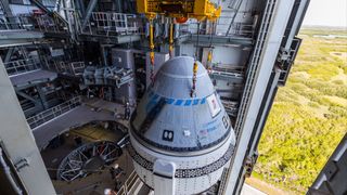 a cone-shaped spacecraft atop a rocket in a large facility.  a large bay is open to the right showing scrub and swamps below