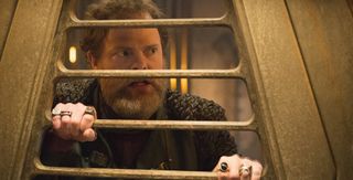 a bearded man looks through a set of metal bars.