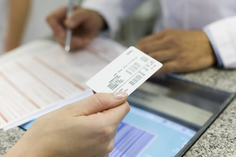 Hand holding insurance card while another person writes on a document