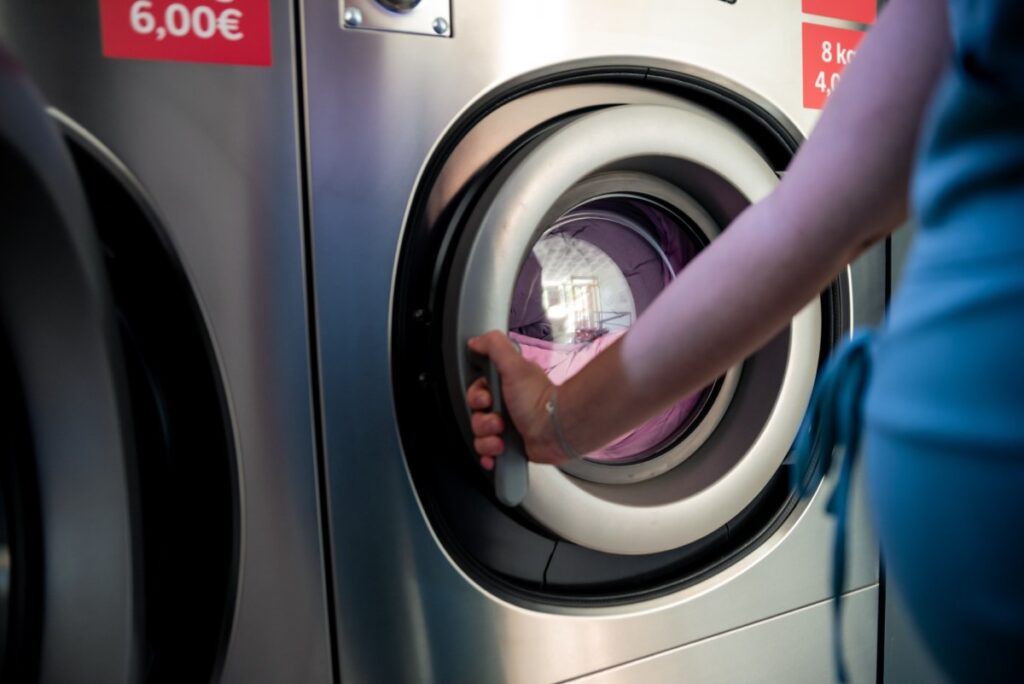 a person's hand closing the door of an industrial washing machine.