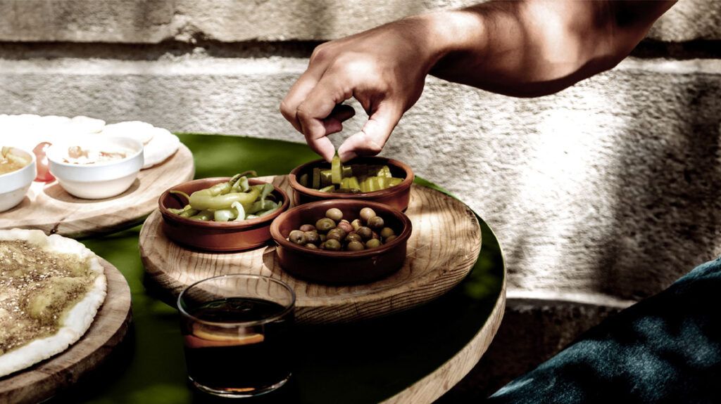 A person picks olive tapas into bowls on a table