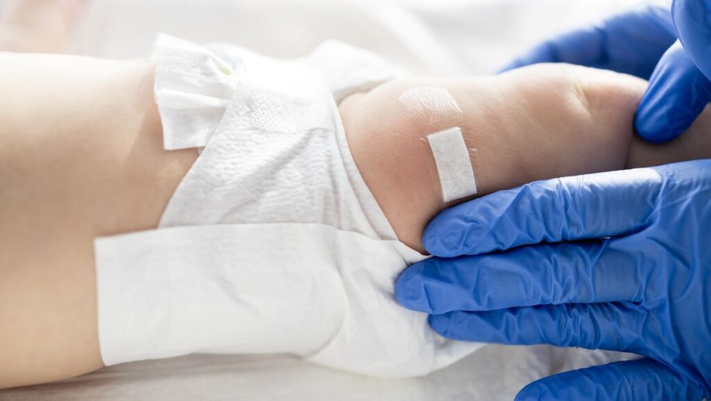 close up on a babies leg as a gloved medical provider places a bandaid on it, as if after a vaccination