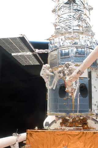 A metal-wrapped spaceship is seen up close.  The astronauts maintain it.