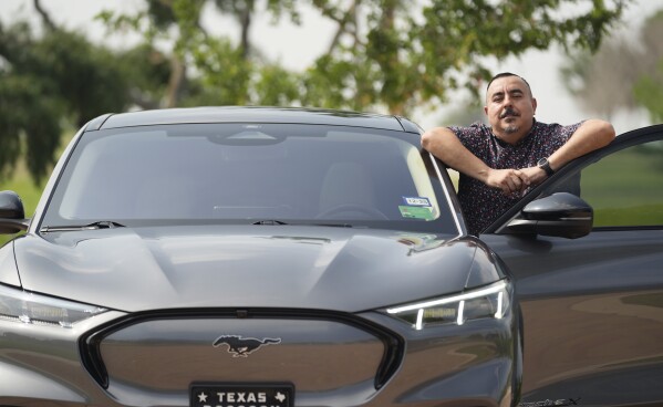 Jose Valdez, 45, owner of three electric vehicles, poses with his Mustang Mach-E, Thursday, May 9, 2024, in San Antonio.  Many Americans still aren't convinced about going electric for their next car purchase.  High prices and a lack of easy-to-find charging stations are major sticking points, according to a new survey.  Valdez owns three electric vehicles, including a new Mustang Mach-E.  With a tax credit and other incentives, the sleek new car costs about $49,000, Valdez said.  He thinks it's worth it.  (AP Photo/Eric Gay)