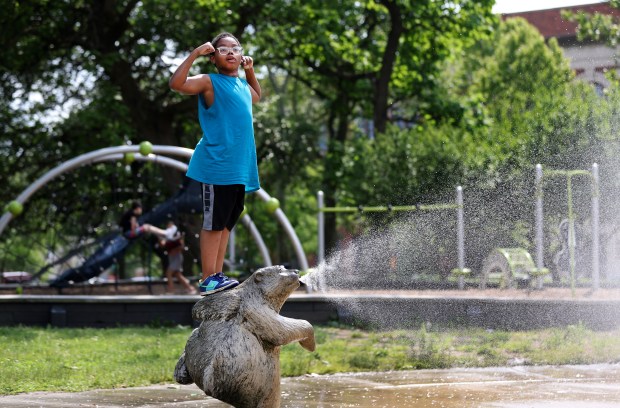 Jacaree Hughes, 9, stands atop a sprinkler as she cools off in Chicago's Douglass Park, June 13, 2024. (Chris Sweda/Chicago Tribune)