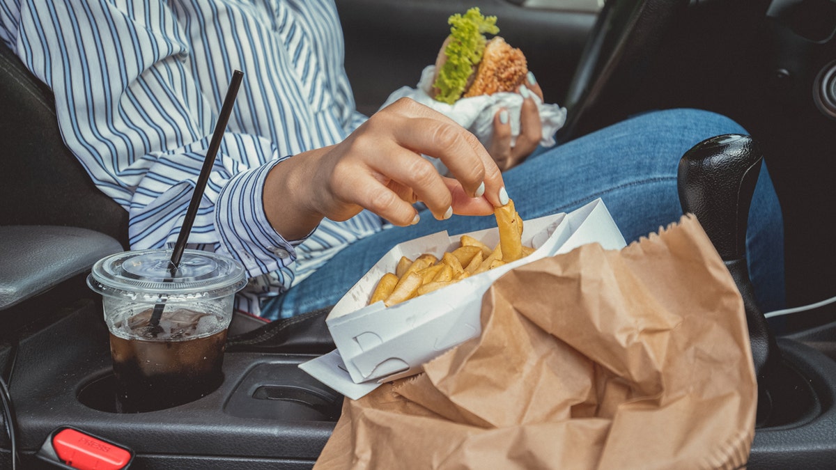 The person eats fries and a hamburger in the car.