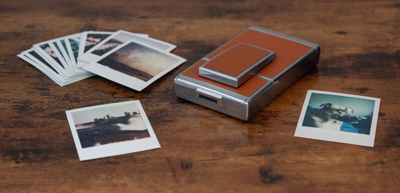 A collection of instant photos scattered across a wooden surface.  On the right, a photo shows a dog.  In the middle is a vintage instant camera with a brown leather cover.  Other photos are partially visible in two stacks on the left side of the camera.