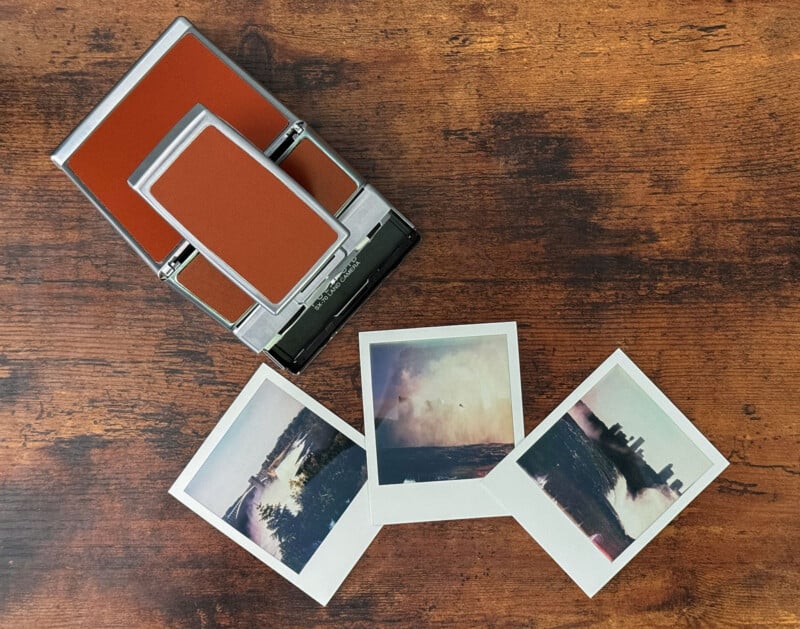 A vintage Polaroid camera with a brown and silver design sits on a wooden surface.  In front of the camera are three snapshots depicting outdoor scenes, including a forest, a body of water, and a cityscape with cloudy skies.