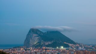 The Rock of Gibraltar at dusk with the Levant Cloud forming above.  In the foreground is the sprawling border town of La Linea de la Concepción, Cádiz, Spain.