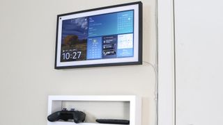 An Amazon Echo Show 15 mounted on a wall in the kitchen with a shelf underneath