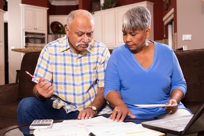 A couple sitting on a couch looking at bills and financial statements on a table in front of them.