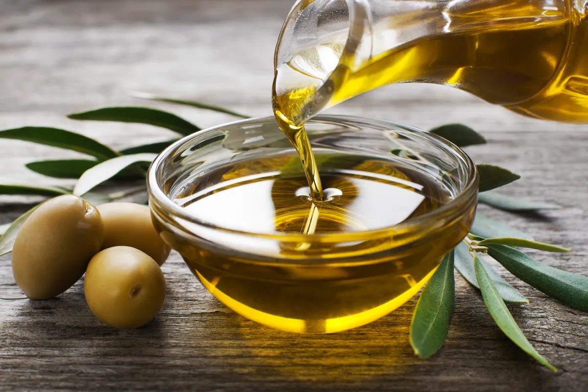 Bottle pouring virgin olive oil into bowl close up