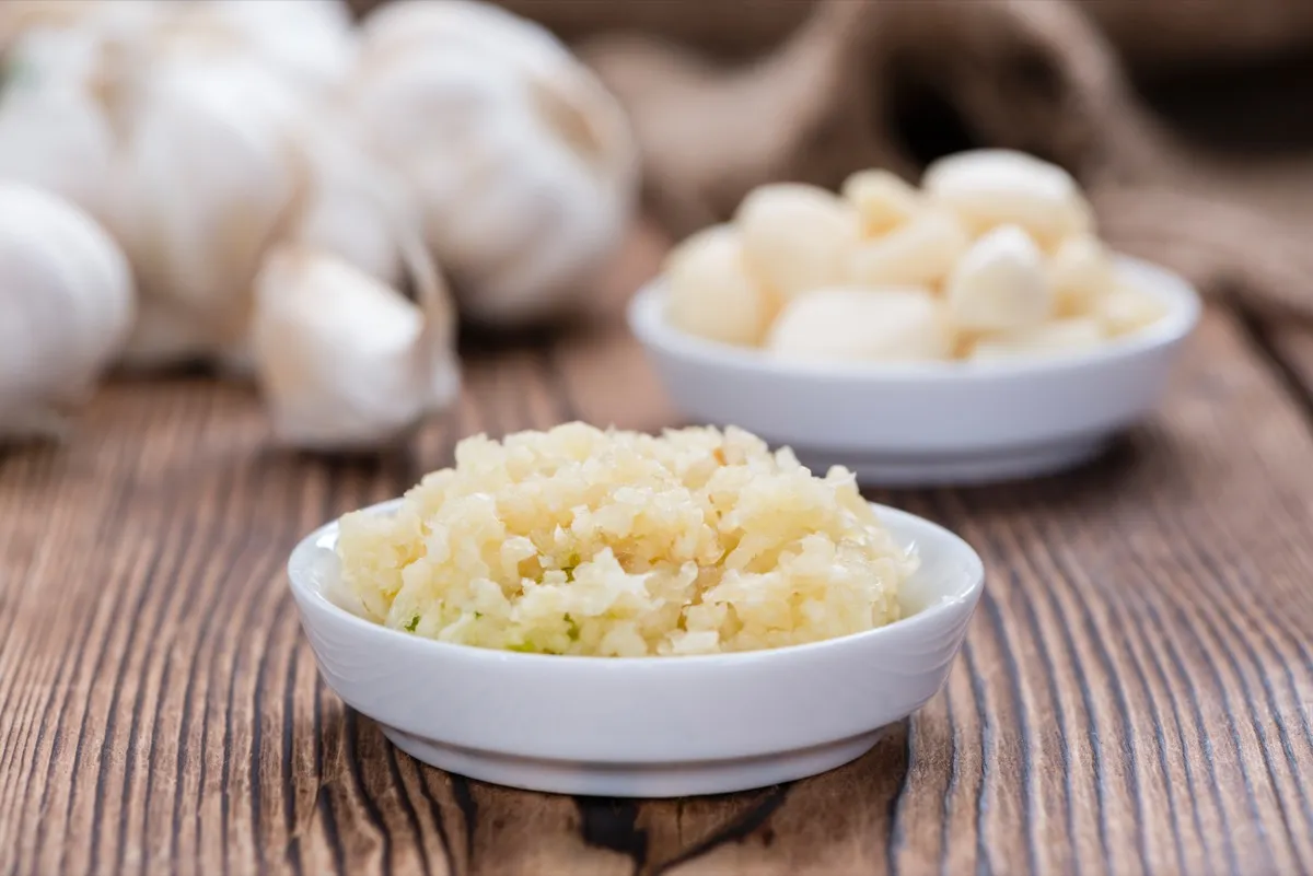 Crushed garlic on a wooden surface with whole garlic in the background