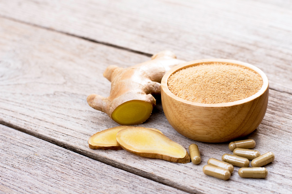 Slice of fresh ginger and powder capsules with ground ginger in wooden bowl isolated on wooden table background. 