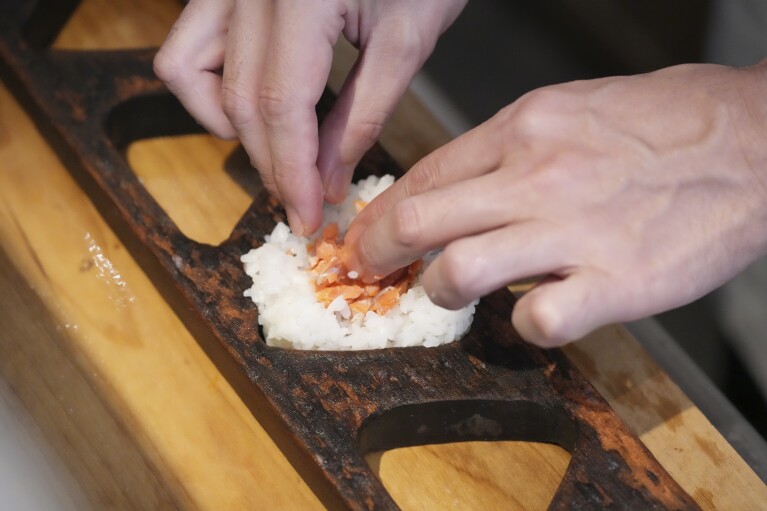 Yosuke Miura prepares a rice ball with pieces of grilled salmon at Onigiri Asakusa Yadoroku, Tokyo's oldest onigiri restaurant, on June 3, 2024, in Tokyo.  Word 