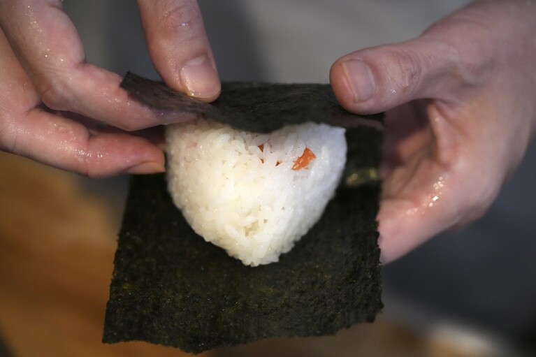 Yosuke Miura wraps seaweed around a rice ball at Onigiri Asakusa Yadoroku, Tokyo's oldest onigiri restaurant, on June 3, 2024, in Tokyo.  Word 