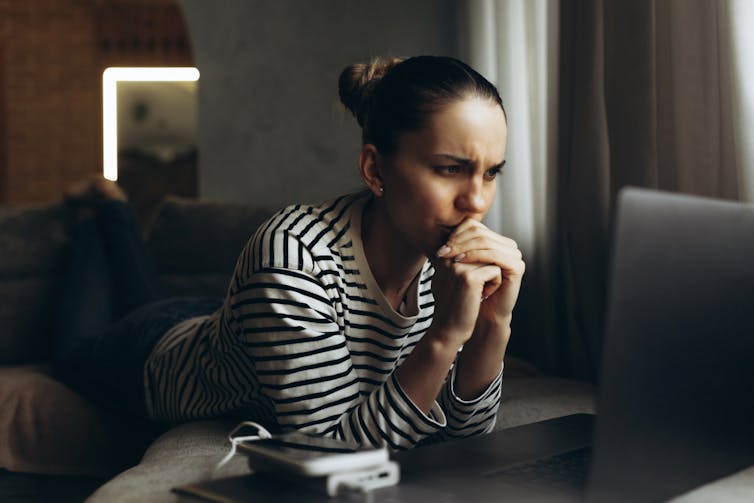 Stressed person looking at a laptop with elbows resting on the surface and hands clasped over mouth