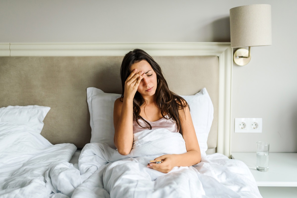 woman lying in bed, not feeling well, with her hand on her head.  Illness/disease concept.  Coronavirus / fever / headache concept.  Home isolation.