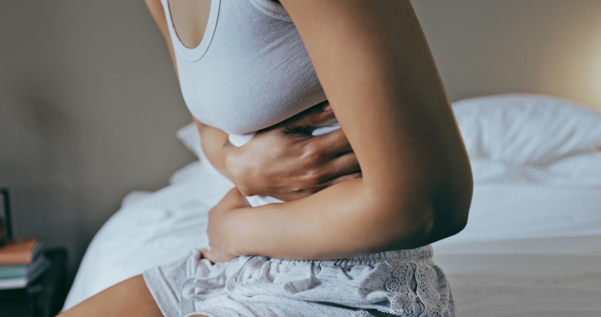 Menstruation, nausea and stomach ache with black woman in bedroom for indigestion, cramps and illness.  Frustrated, gas and stress with girl in bed for constipation, bloating and intestinal problems