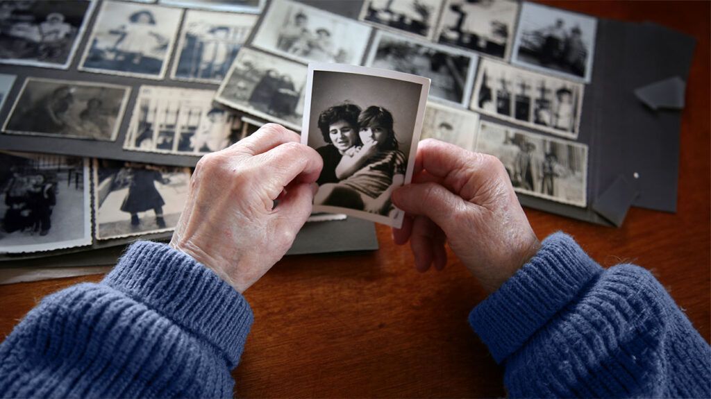 the hands of an elderly person holding a black and white photo of mother and her daughter