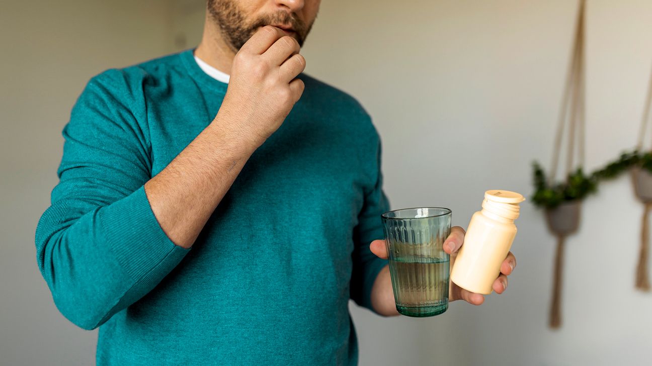 A man taking a pill with a glass of water.