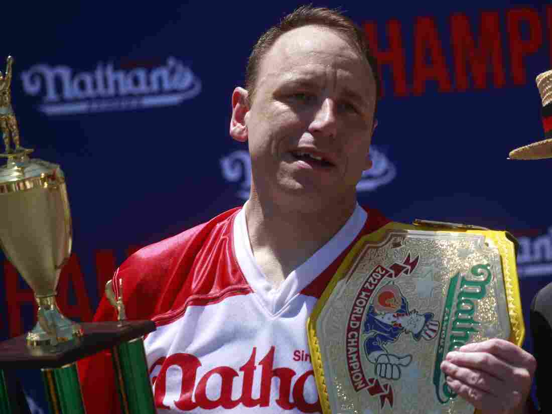 Joey Chestnut holds a trophy and mustard belt after winning the 2022 Nathan's Famous hot dog eating contest.