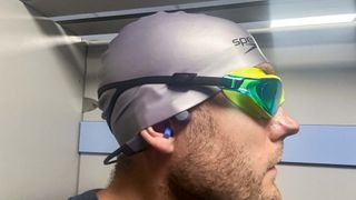 Man wearing the Shokz OpenSwim Pro under a swimming cap