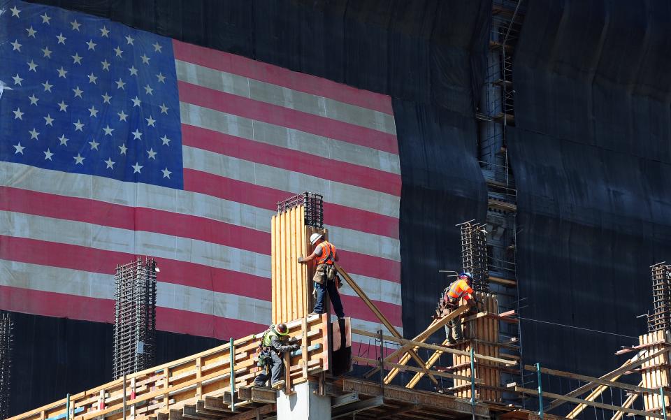 Construction workers work on the construction of a new building partially covered with a large American flag on September 25, 2013 in Los Angeles, California, where state Governor Jerry Brown signed legislation that will raise California's minimum wage from $8 to $10 an hour by 2016. AFP PHOTO/Frederic J. BROWN (Photo credit should read FREDERIC J. BROWN/AFP via Getty Images)