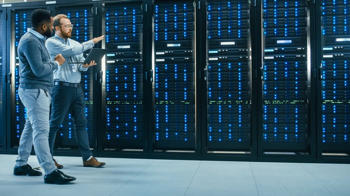 Two people chat as they walk past servers in a data center.