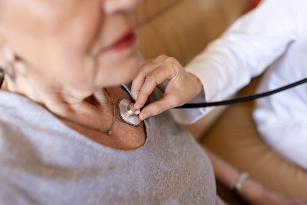 A senior woman has her heartbeat checked by a medical professional with a stethoscope.