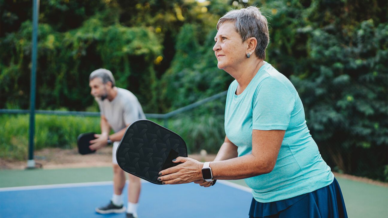 A woman in a blue shirt and a man in a gray shirt are playing pickleball.