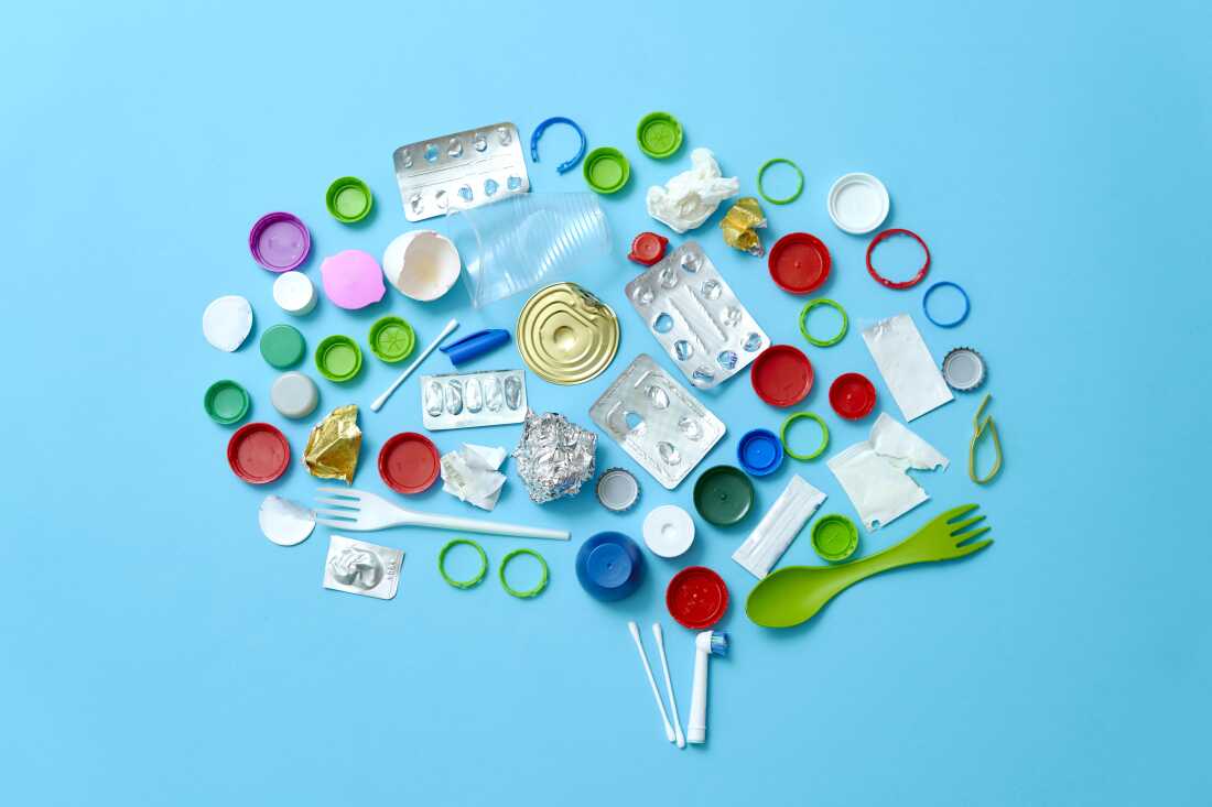 Various colorful trash, such as plastic bottle caps and plastic forks, are arranged in the shape of a human brain, on a light blue background.