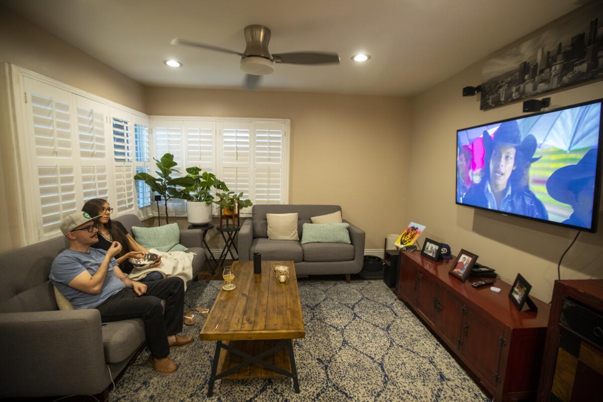 A couple watches a movie on television at their Norwalk home while sharing a bowl of popcorn.