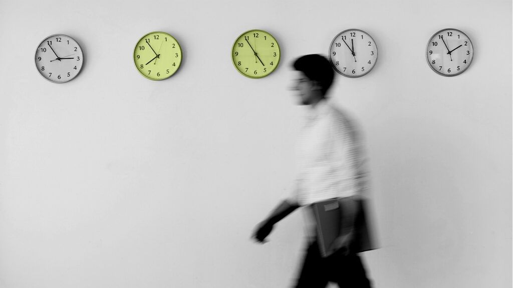 A man walks past five clocks on a wall