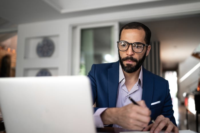 A person holding a pen while looking at a laptop. 