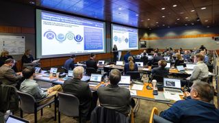 people in professional attire are sitting in a large conference room