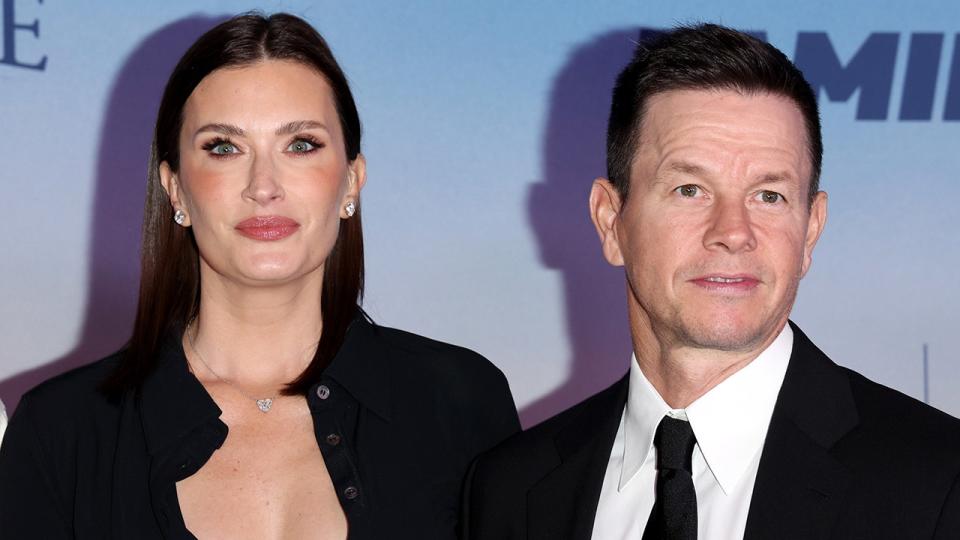 Rhea Durham in a black cardigan smiles sweetly on the red carpet with her husband Mark Wahlberg in a black suit and tie