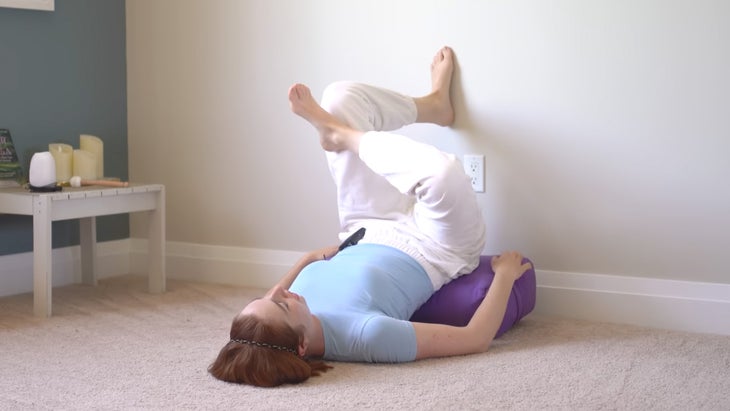 woman practicing yoga against a wall with one foot on the wall