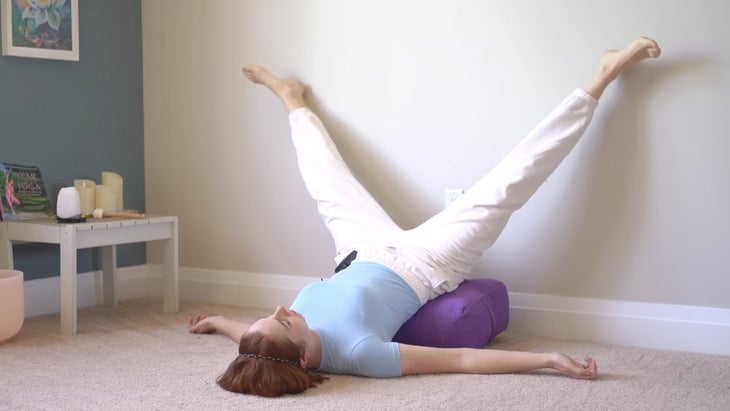 woman practicing yoga against a wall with her feet in a narrow slot