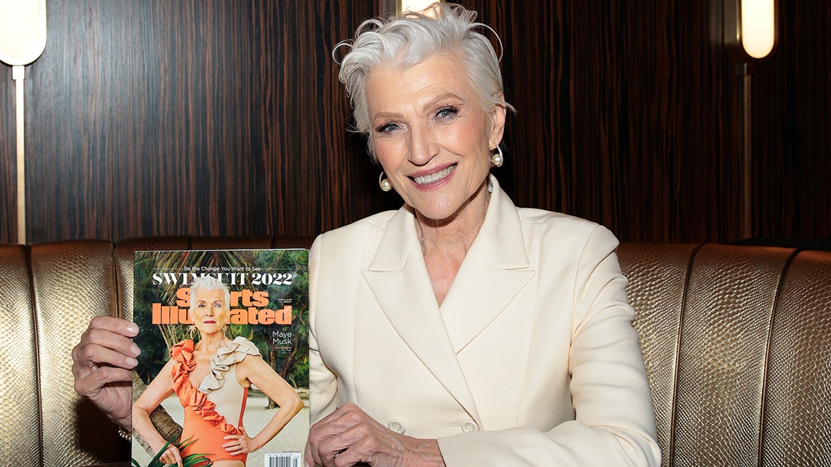 Maye Musk wears a beige suit and holds her SI Swimsuit clutch.