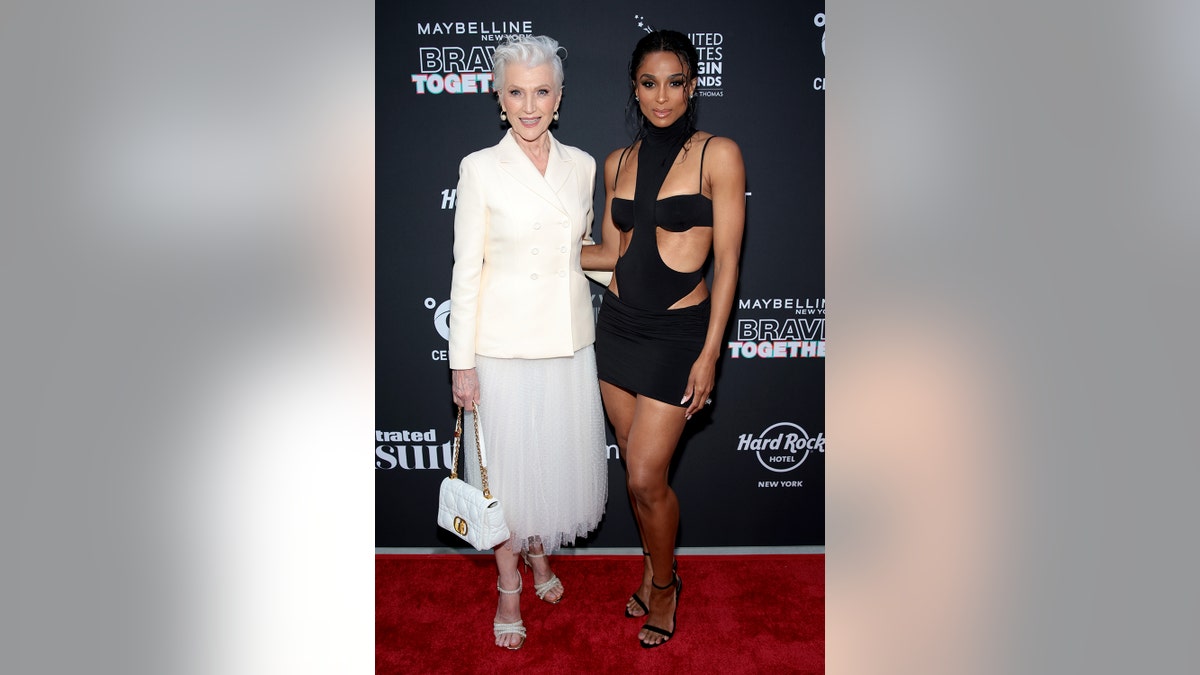 Maye Musk wears a white blazer and white ballerina skirt posing next to Ciara who wears a black cutout dress