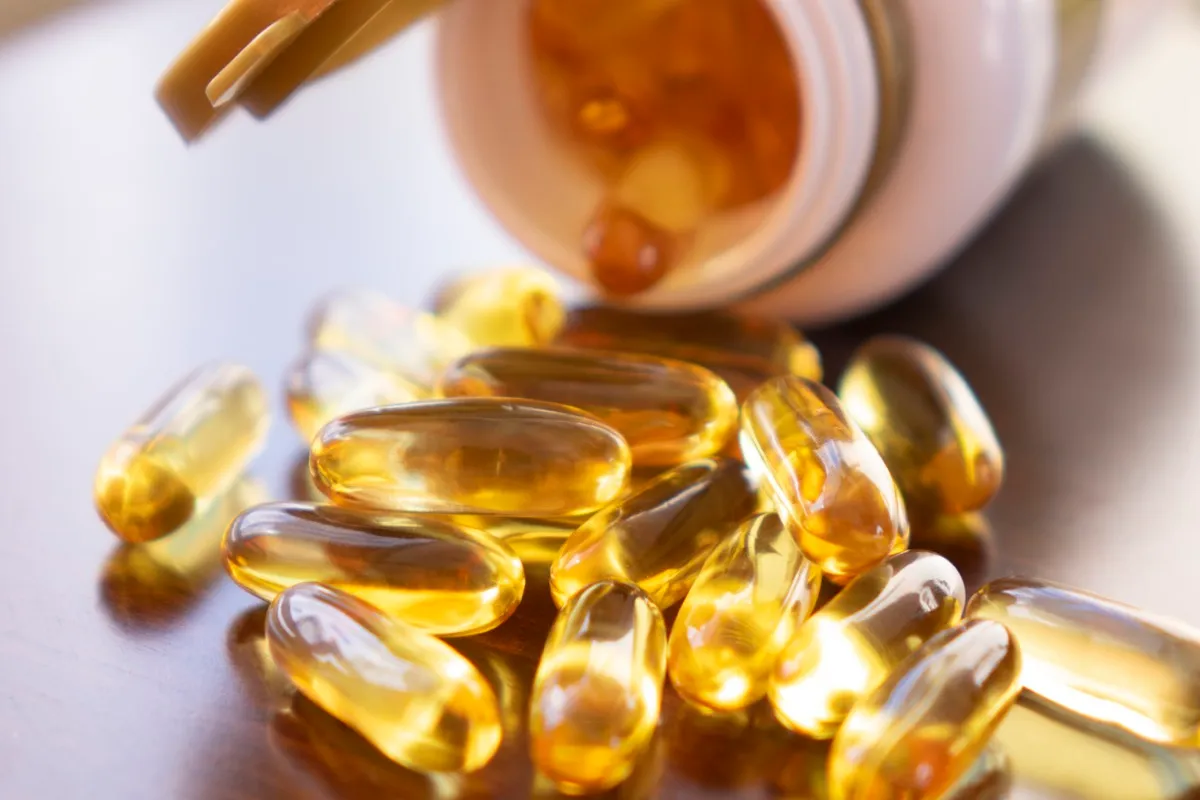 Fish oil capsules with omega 3 and vitamin D in glass bottle on wooden texture, healthy diet concept, close up.