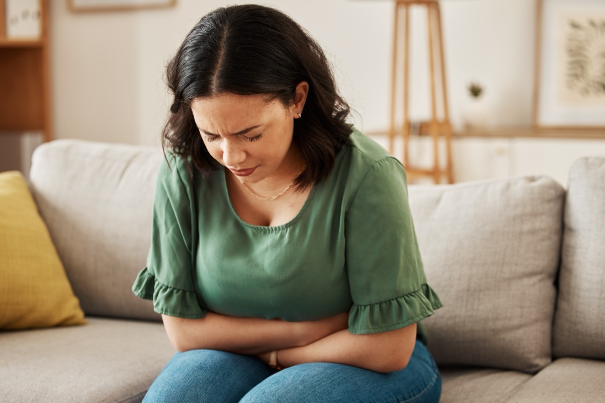 Woman sitting on sofa holding stomach in pain