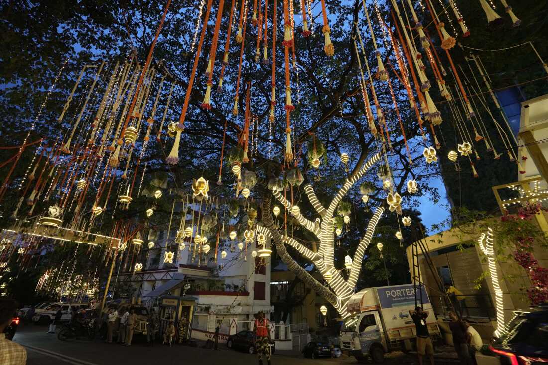 People walk past the Antilia mansion, the home of billionaire Mukesh Ambani, as it is illuminated ahead of the wedding of his son Anant Ambani and Radhika Merchant in Mumbai, India, Wednesday, July 10, 2024. (AP Photo/Rajanish Kakade)