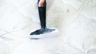 A person steam cleans a white mattress to get rid of bed bug residue