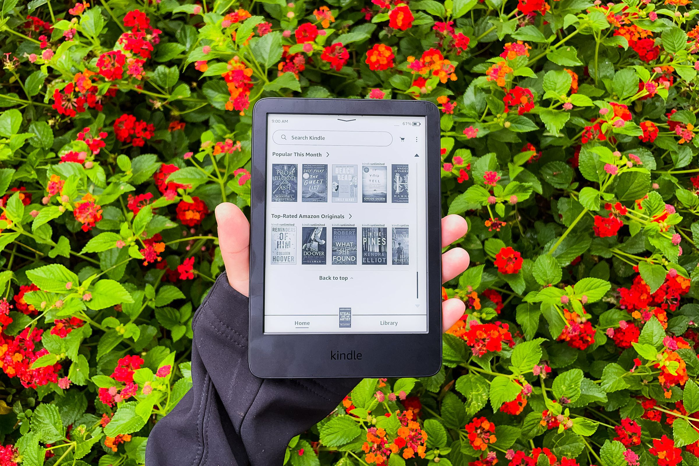 A hand holding Kindle 2022 in front of red flowers.