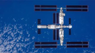 A large T-shaped space station is seen from above with Earth below