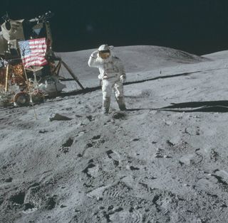 An astronaut in a bulky white spacesuit plants an American flag on the gray, dusty surface of the moon